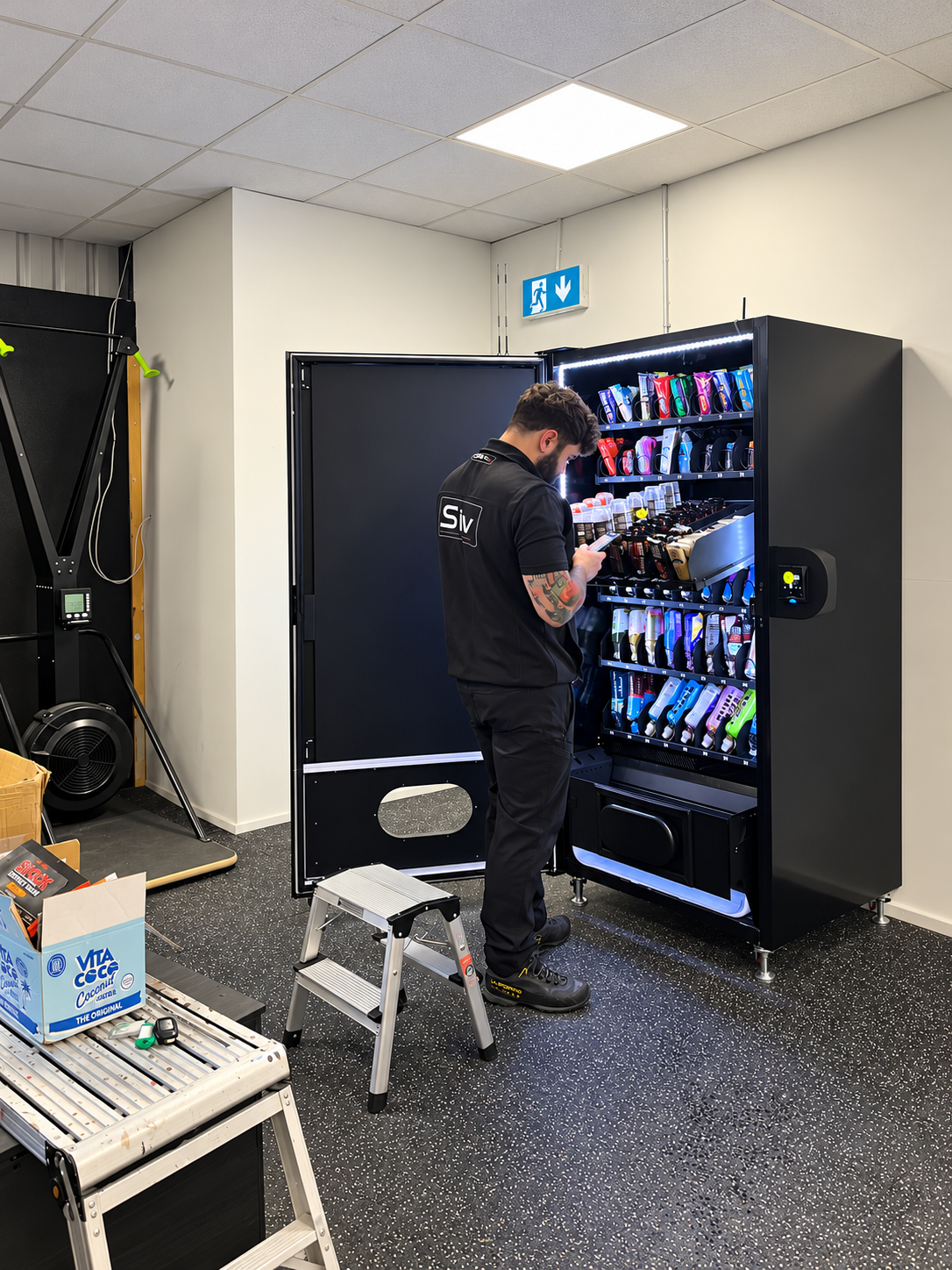 SIV team member servicing a stocked vending machine, with step stool, work platform and product supplies visible.